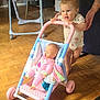 Chloe participe au concours pour gagner de l'argent avec cette photo : toddler, child, baby, toy, doll, stroller, indoor, floor, wooden_floor, person, hand, clothing, play, support, walking, pink, blue, white, happy, home