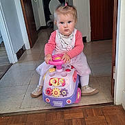 Chloe a rejoint le concours — aidez-le/la à gagner de superbes lots ! baby, child, toy, ride_on_toy, disney, princess, pink, dress, tights, shoes, hair, pony_tail, hallway, floor, door, curious, blue_eyes, indoor, person, playing