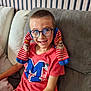 child, boy, glasses, socks, red_tshirt, mickey_mouse, couch, smile, happy, indoor, short_hair, striped_socks, playful, seated, casual_clothing, young, funny_pose, home, furniture, person