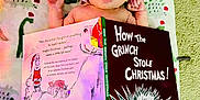 Anakin joined the competition — help win amazing prizes! baby, infant, hat, santa_hat, book, how_the_grinch_stole_christmas, dr_seuss, blanket, dinosaur_pattern, carpet, reading, holiday, christmas, child, cute, indoors, person, face, lying_down, cozy