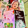 baby, infant, hat, santa_hat, book, how_the_grinch_stole_christmas, dr_seuss, blanket, dinosaur_pattern, carpet, reading, holiday, christmas, child, cute, indoors, person, face, lying_down, cozy