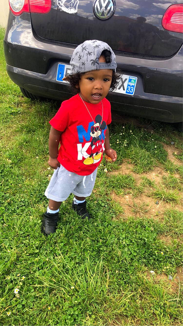 Melvin a rejoint le concours — aidez-le/la à gagner de superbes lots ! auto_part, automotive_design, automotive_exterior, automotive_lighting, automotive_tire, bumper, car, electric_blue, grass, hat, headwear, land_vehicle, landscape, motor_vehicle, person, plant, shoe, sneakers, toddler, trunk