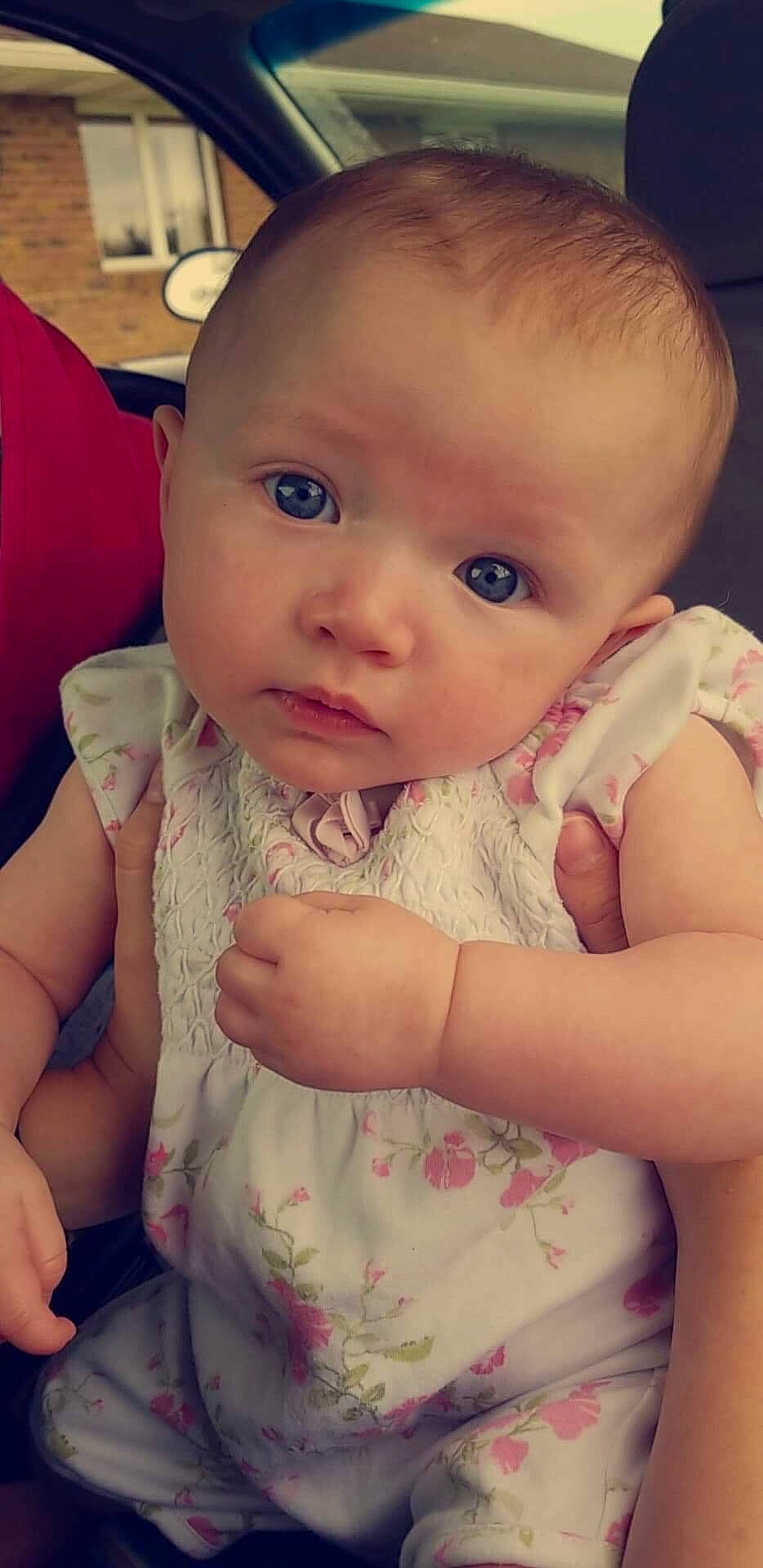 Paisley is registered to the contest to win money with this photo: cheek, child, day, eye, face, finger, girl, hand, head, human_hair_color, infant, iris, lip, mouth, nose, person, pink, sitting, skin, smile