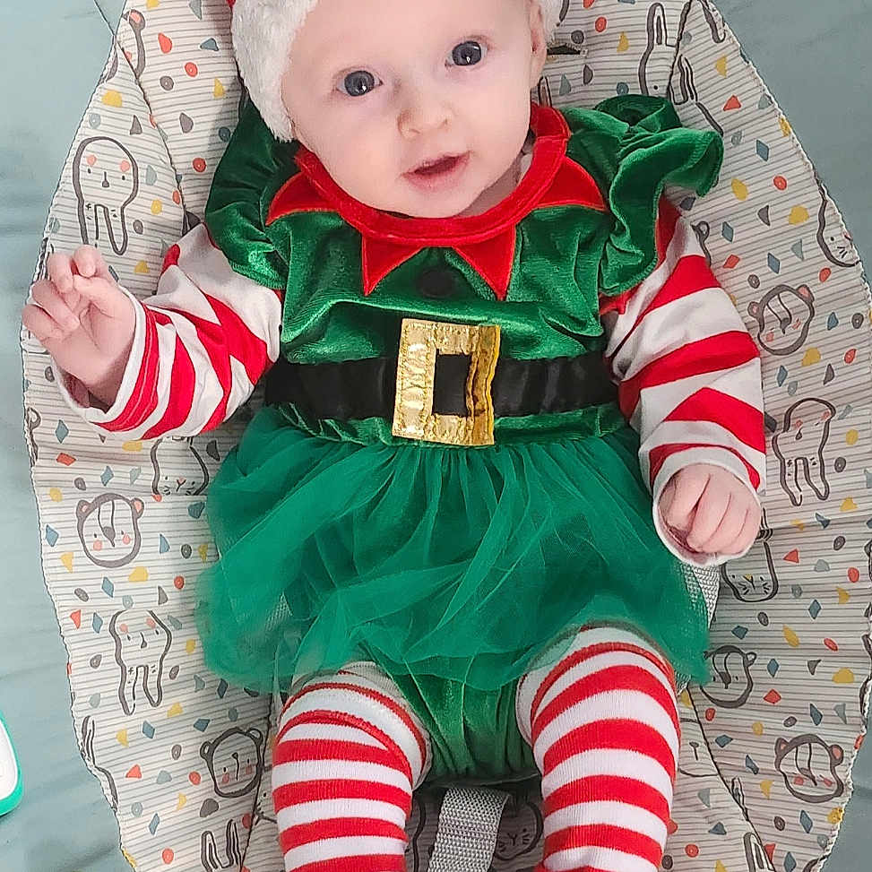 Sofia is registered to the contest to win money with this photo: baby, baby_seat, child, christmas, colorful, cute, elf_costume, festive, green_tutu, holiday, holiday_outfit, indoors, infant, playtime, red_and_white, santa_hat, smiling, soft_toys, striped_clothing, toy