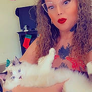 Whiskers is registered to the contest to win money with this photo: arm, blue_eyes, cat, christmas_tree, curly_hair, cute, furniture, glasses, hair, holding, indoor, living_room, person, portrait, red_lipstick, selfie, stocking, tattoo, tv, white_cat