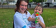 Greyson is registered to the contest to win money with this photo: teenager, toddler, water_gun, smiling, outdoor, park, grass, trees, wet_hair, casual_clothing, braces, joyful, holding, child, playing, fun, daytime, person, happy, urban_background