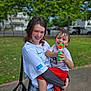 teenager, toddler, water_gun, smiling, outdoor, park, grass, trees, wet_hair, casual_clothing, braces, joyful, holding, child, playing, fun, daytime, person, happy, urban_background