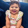 accessory, baby, blue_couch, bracelet, child, chubby_cheeks, clothing, couch, cute, floral_top, happy, indoor, infant, joyful, person, pigtails, pink_shorts, portrait, sitting, smiling