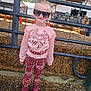 child, girl, sunglasses, pink_sweater, patterned_pants, cowboy_boots, farm, fence, hay_bales, barn, outdoor, sunny, smiling, standing, person, casual_clothing, daytime, rural, young_child, confident
