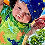 baby, child, water, splash, hat, blue_hat, dinosaur_shirt, green_shirt, outdoor, sunny, hand_holding, water_droplets, playtime, summer, happy, cute, infant, person, closeup, fun