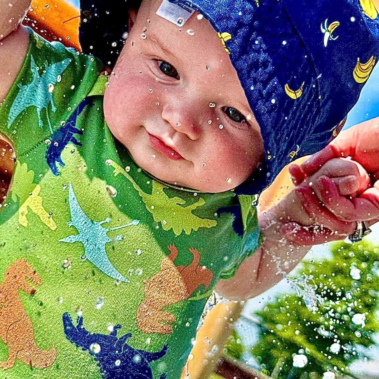 Gatlin joined the competition — help win amazing prizes! baby, blue_hat, child, closeup, cute, dinosaur_shirt, fun, green_shirt, hand_holding, happy, hat, infant, outdoor, person, playtime, splash, summer, sunny, water, water_droplets