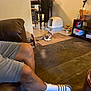 cat, person, legs, shorts, sock, sandals, couch, living_room, floor_mat, litter_box, chair, table, shelf, bottle, cross, carpet, indoor, home, relaxing, furniture