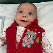 Rustyn is registered to the contest to win money with this photo: baby, infant, red_vest, bear_embroidery, smile, cute, happy, child, clothing, blanket, portrait, face, wide_eyes, indoor, soft_light, zipped_vest, patterned_onesie, young_child, close_up, cozy