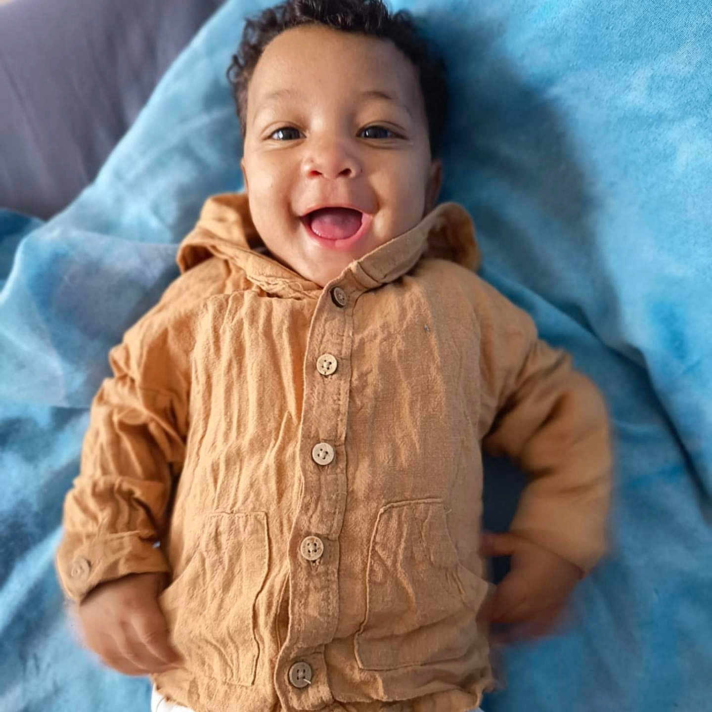 Lamine participe au concours pour gagner de l'argent avec cette photo : baby, blanket, buttoned_jacket, child, clothing, cute, fabric, face, happy, head, indoors, infant, jacket, lying_down, pants, person, portrait, smile, soft_texture, young