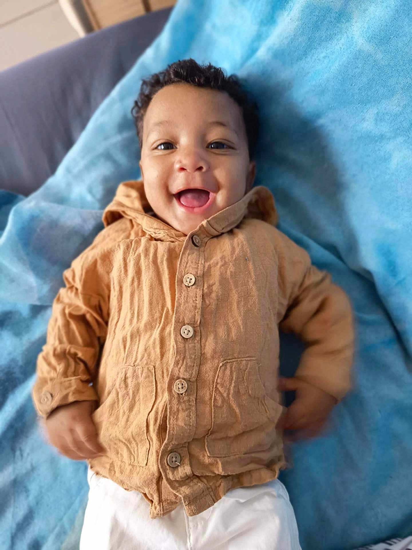 Lamine participe au concours pour gagner de l'argent avec cette photo : baby, child, smile, happy, clothing, jacket, pants, blanket, fabric, person, portrait, cute, infant, lying_down, indoors, buttoned_jacket, soft_texture, face, head, young