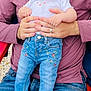 baby, child, person, adult, hands, jeans, embroidered_clothing, socks, white_shirt, outdoor, grass, red_chair, holding, casual_clothing, seated, close_up, portrait, skin, face, gentle