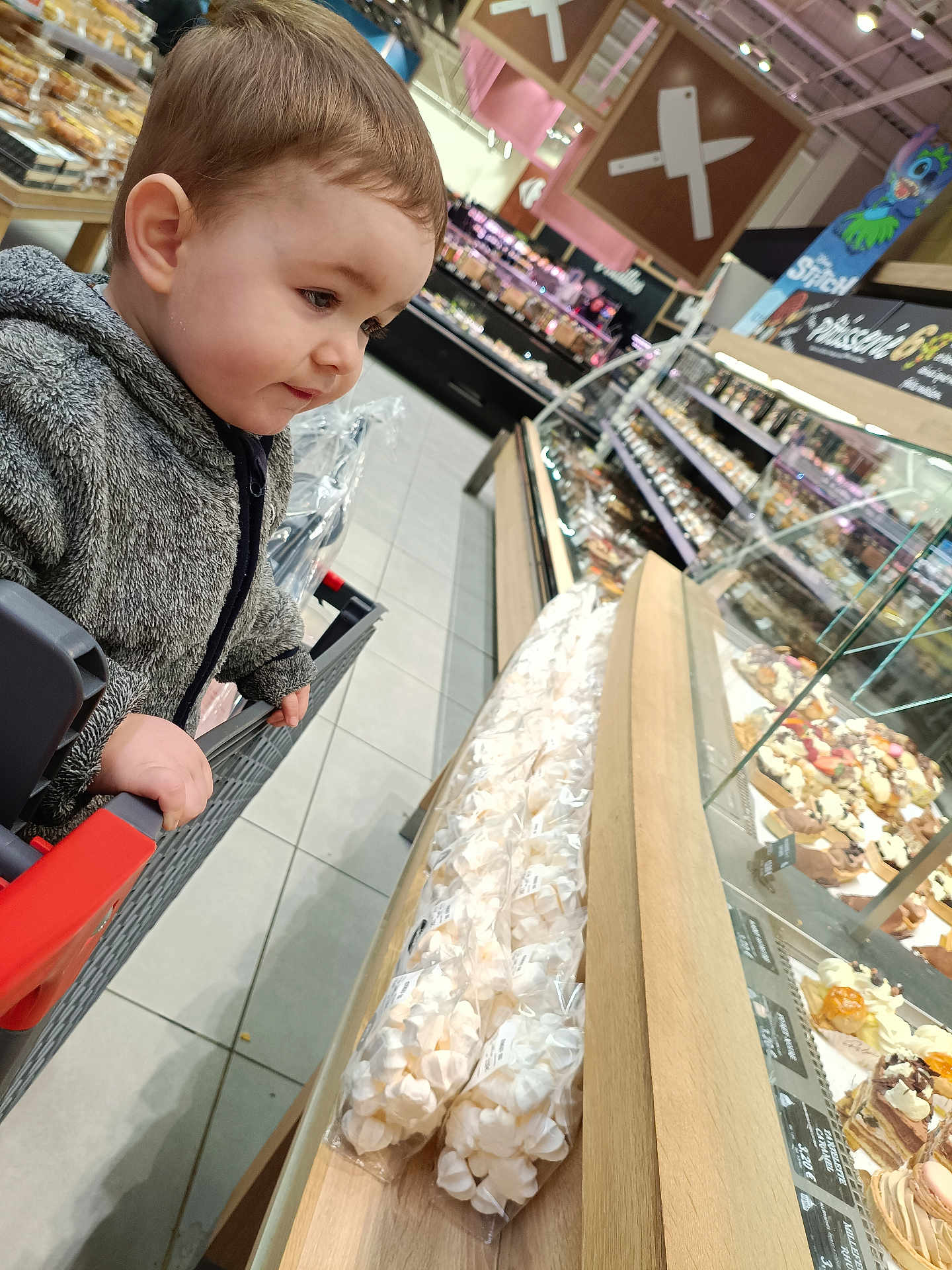 Gauthier a rejoint le concours — aidez-le/la à gagner de superbes lots ! toddler, child, shopping_cart, bakery, pastries, supermarket, food_display, glass_case, cozy_jacket, curious, indoors, floor_tiles, handrail, snack, dessert, bread, store, shopping, grocery, bakery_section