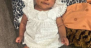 Madolyn joined the competition — help win amazing prizes! baby, infant, child, white_dress, socks, couch, pillow, patterned_pillow, leopard_print, orange_pillow, brown_pillow, carpet, indoor, person, cute, smile, face, curly_hair, relaxing, portrait