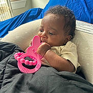 Madolyn joined the competition — help win amazing prizes! baby, infant, teething_toy, pink_toy, blanket, curly_hair, indoor, window, natural_light, blue_fabric, cute, child, person, relaxing, soft_lighting, cozy, portrait, young_child, resting, baby_toy
