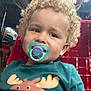 Filip is registered to the contest to win money with this photo: toddler, child, pacifier, curly_hair, red_seat, teal_shirt, moose_graphic, indoor, portrait, closeup, young_child, cute, sitting, face, expression, baby, seat, transport, casual, clothing