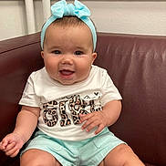 Sienna Rose is registered to the contest to win money with this photo: baby, child, smiling, headband, blue, shorts, white_shirt, leopard_print, sitting, couch, leather, happy, indoor, cute, infant, portrait, person, skin, hand, face
