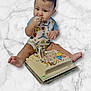 baby, child, cake, birthday_cake, sprinkles, candle, onesie, frosting, sitting, celebration, smiling, cute, hands, feet, marble_surface, food, party, colorful, infant, eating
