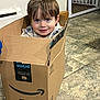 child, boy, cardboard_box, amazon, prime, indoor, floor, tile_floor, smiling, happy, cute, playful, home, person, young_child, packaging, cardboard, casual_clothing, blue_eyes, short_hair