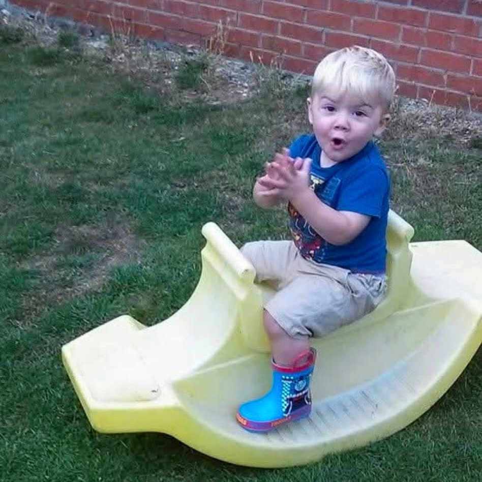 Kaidenmoore joined the competition — help win amazing prizes! backyard, blue, boots, brick_wall, child, clapping, fence, fun, grass, happy, outdoor, plastic, play, rocking_toy, shorts, summer, toddler, toy, tshirt, yellow