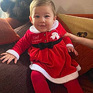 Emma participe au concours pour gagner de l'argent avec cette photo : baby, child, red_dress, festive_clothing, couch, cat, hand, indoor, smiling, person, holiday, cozy, plush, furniture, cushion, toddler, warm_lighting, fur, pet, portrait