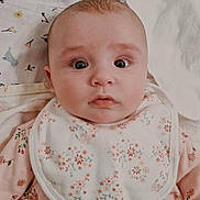 Kiara joined the competition — help win amazing prizes! baby, infant, face, eyes, bib, pajamas, floral_pattern, bed, blanket, sheet, laying_down, skin, cute, child, person, young, indoors, soft_lighting, expression, clothing