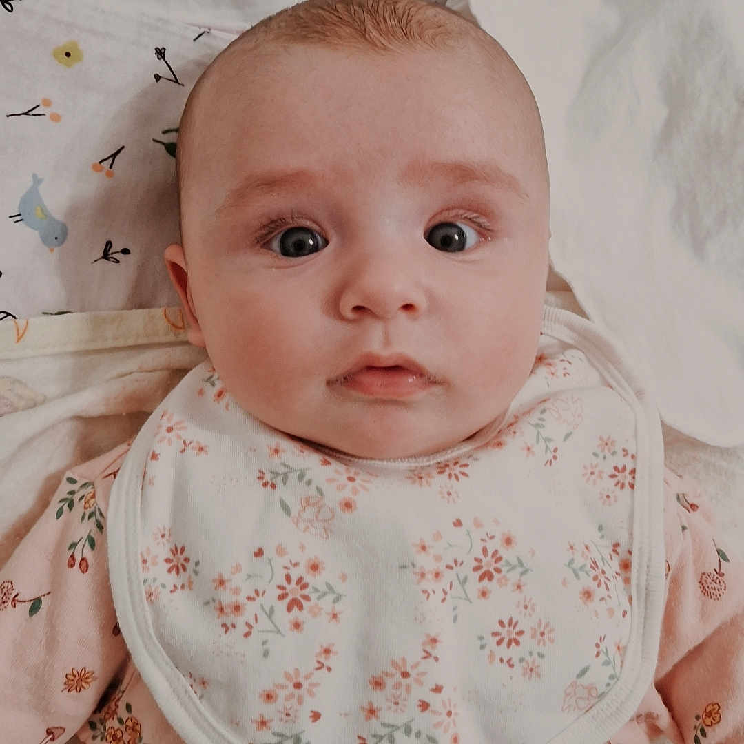 Kiara joined the competition — help win amazing prizes! baby, bed, bib, blanket, child, clothing, cute, expression, eyes, face, floral_pattern, indoors, infant, laying_down, pajamas, person, sheet, skin, soft_lighting, young