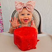 Freya is registered to the contest to win money with this photo: baby, child, high_chair, bow, watermelon, fruit, happy, smiling, hand, face, cute, food, summer, pink, patterned_curtain, jewelry, bracelet, indoor, portrait, toddler