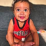 baby, child, infant, smiling, red_clothing, sitting, couch, indoors, cute, portrait, happy, face, feet, hand, skin, curly_hair, tank_top, expression, young, person