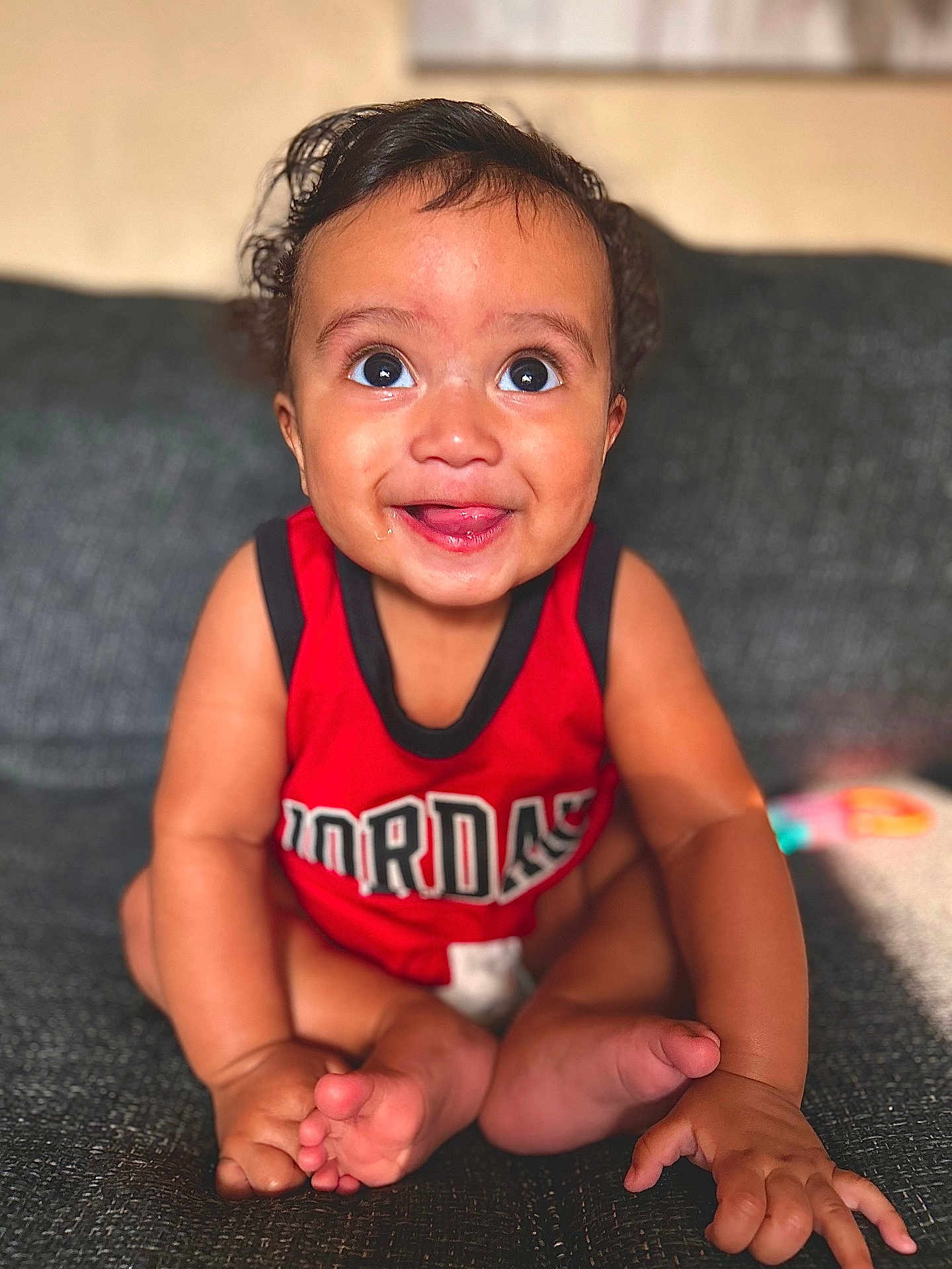 Isaiah J Anderson is registered to the contest to win money with this photo: baby, child, infant, smiling, red_clothing, sitting, couch, indoors, cute, portrait, happy, face, feet, hand, skin, curly_hair, tank_top, expression, young, person