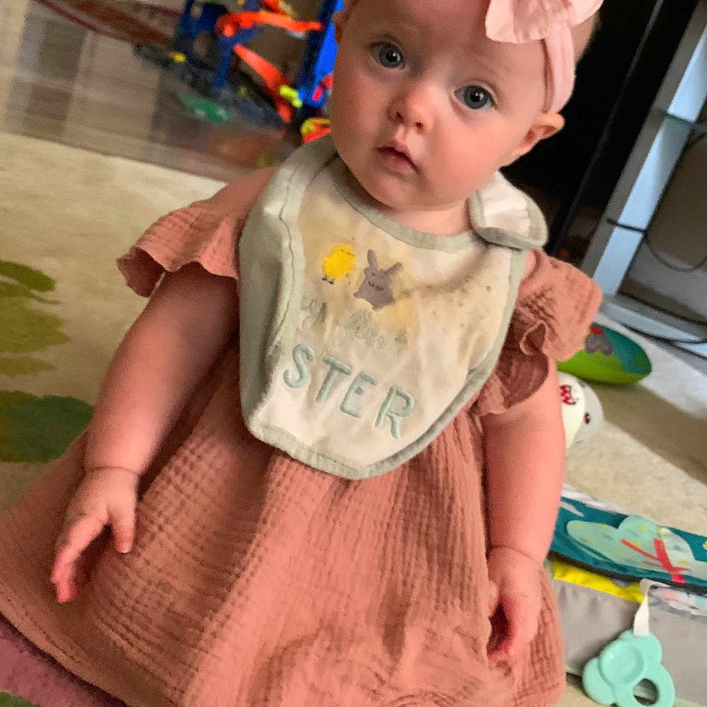Starlite is registered to the contest to win money with this photo: baby, bib, carpet, child, curious, cute, dress, expression, floor, footwearless, headband, home, indoor, infant, person, pink_bow, playtime, sitting, toys, young_child