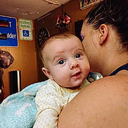 Juniper is registered to the contest to win money with this photo: baby, adult, indoor, person, face, blanket, wall, sign, poster, shoulder, hair, skin, clothing, holding, curious, closeup, room, decor, child, expression