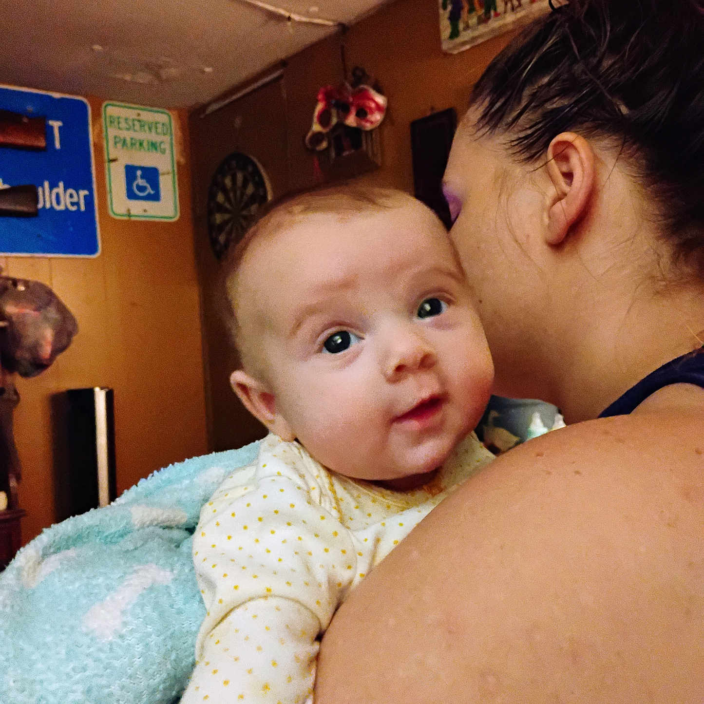 Juniper is registered to the contest to win money with this photo: adult, baby, blanket, child, closeup, clothing, curious, decor, expression, face, hair, holding, indoor, person, poster, room, shoulder, sign, skin, wall