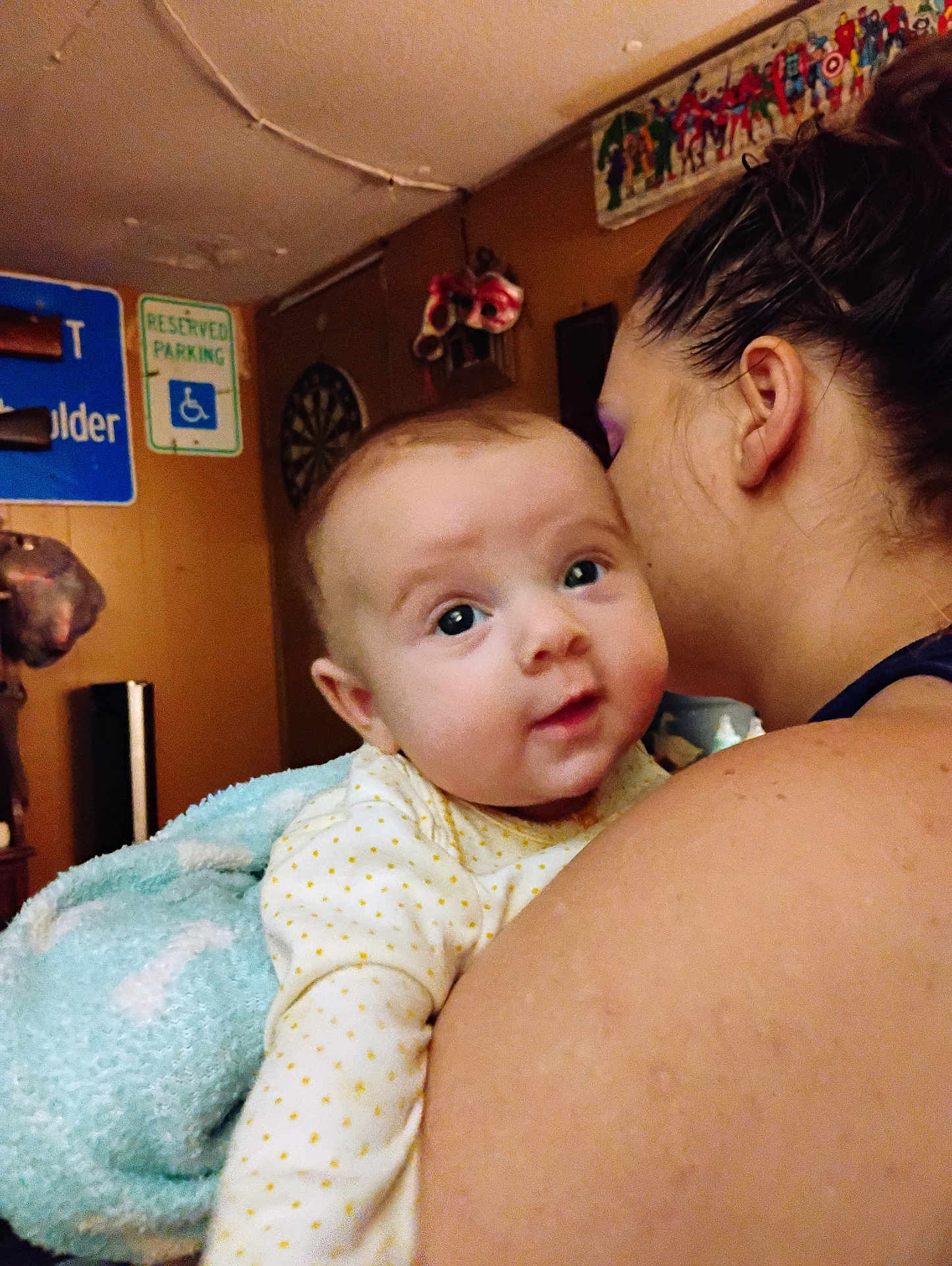 Juniper is registered to the contest to win money with this photo: baby, adult, indoor, person, face, blanket, wall, sign, poster, shoulder, hair, skin, clothing, holding, curious, closeup, room, decor, child, expression