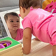 Milani joined the competition — help win amazing prizes! baby, child, childhood, crawling, curiosity, cute, development, early_learning, earring, face, indoor, infant, mirror, pink_clothing, play_mat, reflection, smile, toddler, toy, wooden_box