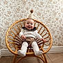 baby, smiling, party_hat, rattan_chair, floral_wallpaper, wooden_floor, white_tights, brown_shorts, white_sweater, indoor, cute, happy, child, portrait, celebration, half_birthday, furniture, home, cozy, decor