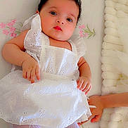 Liya is registered to the contest to win money with this photo: baby, child, infant, white_dress, tights, lying_down, bed, floral_pattern, hand, cute, face, portrait, indoors, soft_lighting, fabric, sleepwear, baby_clothing, resting, newborn, person
