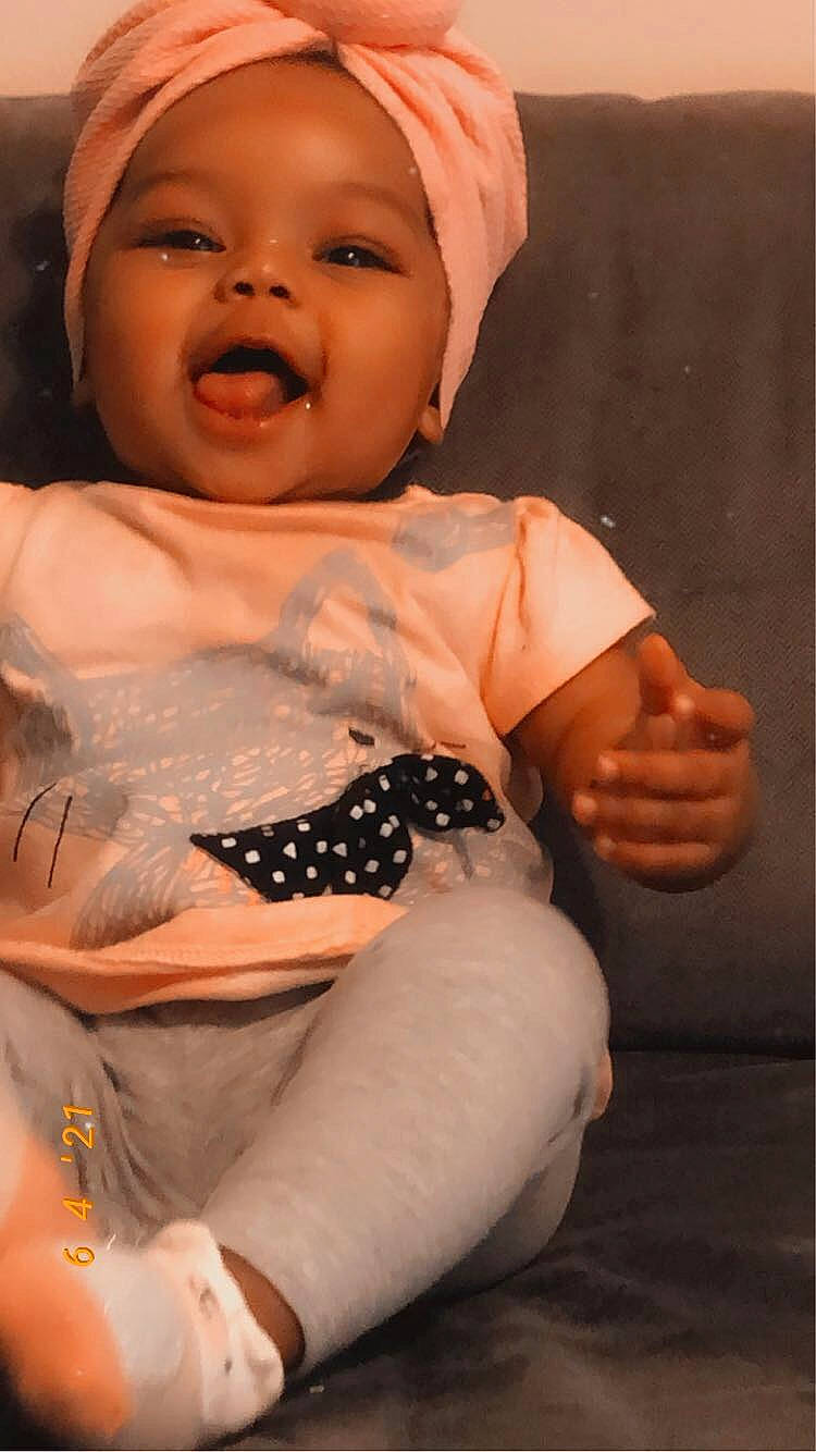 Leilani is registered to the contest to win money with this photo: arm, baby, baby_toddler_clothing, comfort, dress, eye, finger, gesture, hand, happy, headwear, human_body, lip, mouth, nose, person, skin, sleeve, smile, thigh