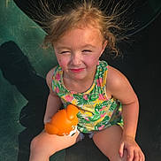 Hayzlee is registered to the contest to win money with this photo: child, girl, toy, orange_toy, hair, static_hair, sunlight, shadow, sitting, floral_top, shorts, playground, outdoor, summer, skin, face, expression, person, cute, happy