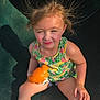 child, girl, toy, orange_toy, hair, static_hair, sunlight, shadow, sitting, floral_top, shorts, playground, outdoor, summer, skin, face, expression, person, cute, happy