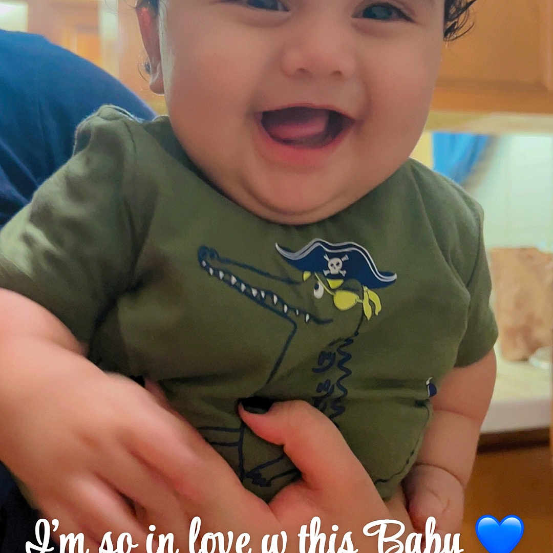 Jaziel is registered to the contest to win money with this photo: baby, child, smiling, curly_hair, green_shirt, pirate_graphic, indoor, kitchen, person, happy, holding, hand, cute, portrait, infant, closeup, cheerful, face, young_child, expression