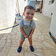 Samuel participe au concours pour gagner de l'argent avec cette photo : child, toddler, smiling, outdoor, stone_patio, overalls, striped_shirt, sandals, happy, standing, sunlight, daylight, playful, young_child, casual_clothing, portrait, person, summer, vacation, home