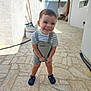 child, toddler, smiling, outdoor, stone_patio, overalls, striped_shirt, sandals, happy, standing, sunlight, daylight, playful, young_child, casual_clothing, portrait, person, summer, vacation, home