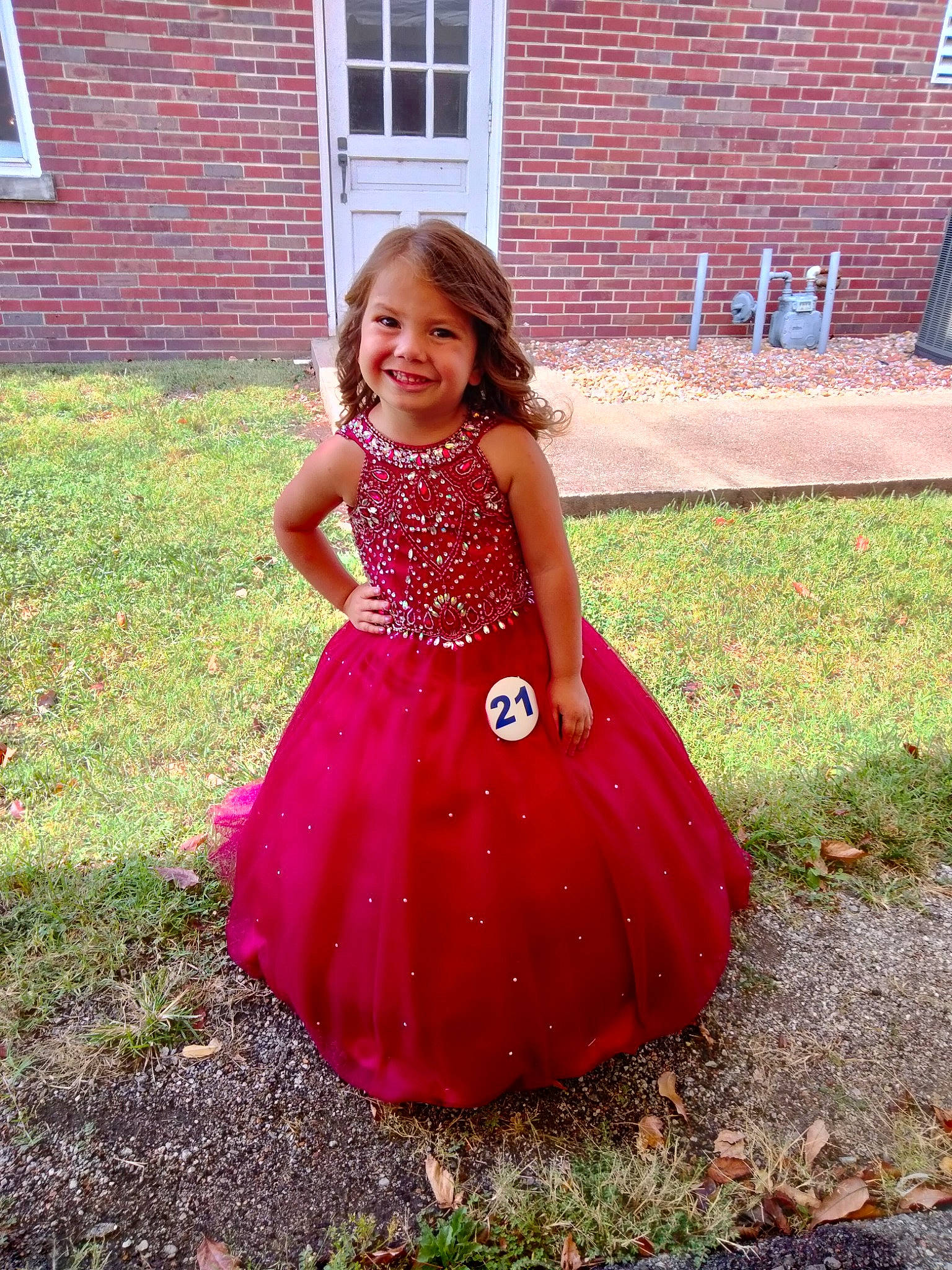 Josie is registered to the contest to win money with this photo: arm, day_dress, dress, eye, grass, hair, happy, head, house, human_body, joy, one_piece_garment, people_in_nature, person, pink, plant, shoulder, smile, toddler, tree