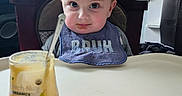 Jasper is registered to the contest to win money with this photo: baby, infant, child, high_chair, bib, bruh, face, blue_eyes, blond_hair, sitting, indoor, kitchen, shelf, food, snack, spoon, cup, table, portrait, messy_meal