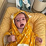 baby, basket, blanket, child, cozy, curious_expression, cushion, cute, footwear, hand, hooded_towel, indoor, infant, open_mouth, person, plush_toy, soft_fabric, white_dots, wooden_floor, yellow_towel